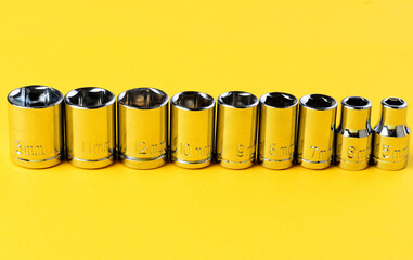 Set of chrome socket wrench heads arranged in row on yellow background close up