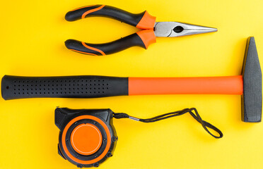 Top view of hammer measuring tape and pliers on yellow background construction tools