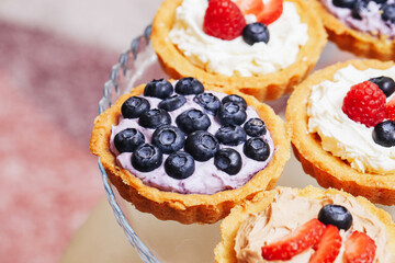 Mini fruit tartlets on glass plate. Sweet dessert with cream and berries. Blueberries, raspberries...