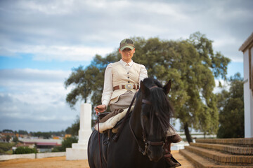 Young female horsewoman riding a black Spanish thoroughbred horse, trotting with him towards the...