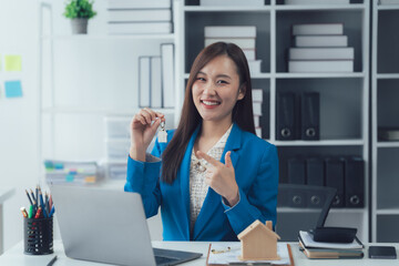 Real Estate Agent with House Key: A smiling agent holds up a house key in her office, beside a...