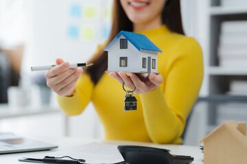 Dream Home Showcase: A woman joyfully presents a miniature house, holding a pen to emphasize the...