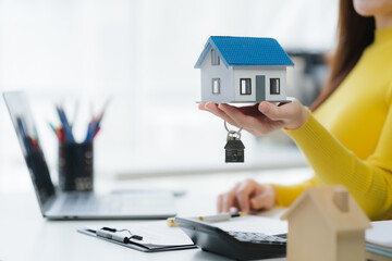 Home ownership concept: A detailed shot reveals a person's hand holding a miniature house and keys,...