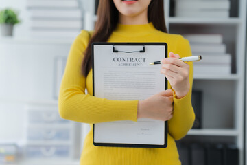 Negotiating a Contract: A poised businessperson in a stylish yellow blouse meticulously reviews and...