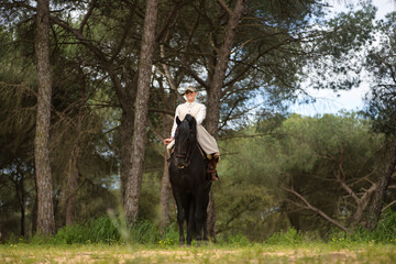 Young horsewoman riding her black Spanish thoroughbred horse, posing in the middle of the field....