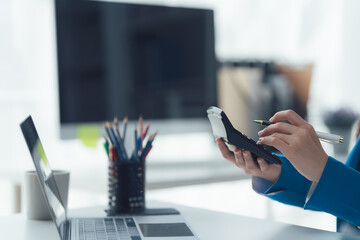  Calculating in the Office: Focused hands manipulate a calculator at a modern workstation, with a laptop, pens.