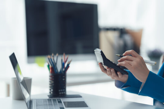  Calculating in the Office: Focused hands manipulate a calculator at a modern workstation, with a laptop, pens.