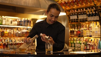 Profile good looking Asian bartender using jigger measure liquor syrup into glass with rock ice at luxurious beverage counter bar scene, neat professional barman costume at nightclub luxury. Vinosity.