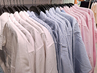 Neatly arranged pastel-colored and striped shirts hang on a clothing rack in a store, showcasing a variety of summer styles ready for purchase.