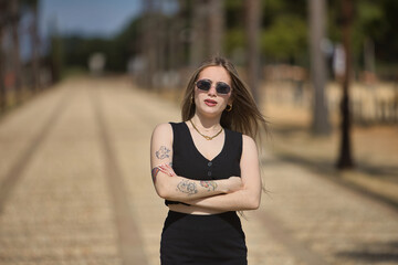 Young, beautiful, blonde woman, with black top and skirt and sunglasses, with her arms crossed,...