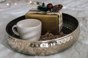 Cozy winter arrangement with a gift and a warm cup on a decorative tray in soft lighting