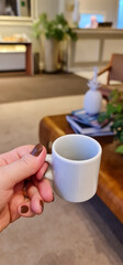 A woman's hand holding a small empty coffee cup in a cozy, modern setting. The scene conveys a sense of comfort and relaxation.