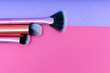 Colorful makeup brushes arranged on vibrant pink and purple background
