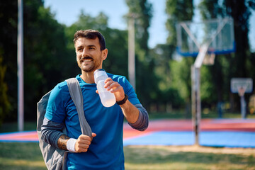 Happy athletic man drinking water after sports training outdoors.