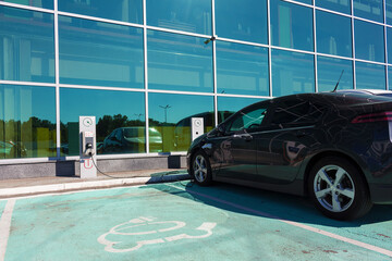 Electric car charging at modern EV charging station in designated green parking spot with clearly...