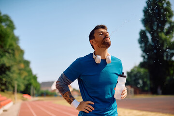 Athletic man spitting water while exercising outdoors.