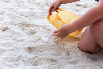 Individual is kneeling on sandy beach, carefully picking up litter with a yellow bag, showcasing commitment to environmental protection and cleanliness, encouraging others to maintain clean beaches