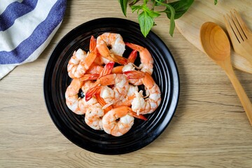 Boiled shrimp in black  ceramic plate on wooden background , top view food table 