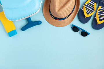 Kids beach summer frame from suitcase, sun protection cream, straw hat, sandals and sunglasses on blue background. Top view. Copy space