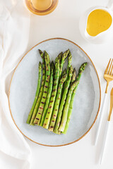 Grilled green asparagus on plate with hollandaise sauce on white table. Top view