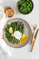 Poached egg with grilled asparagus, spinach, and hollandaise sauce on white table. Top view