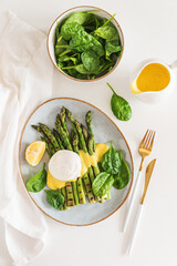 Poached egg with grilled asparagus, spinach, and hollandaise sauce on white table. Top view