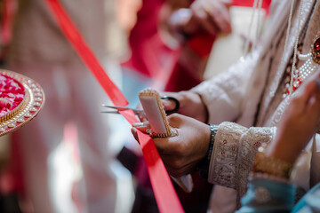 Couple at Indian Wedding Cutting Ribbon, detail shot. Focus on hands cutting red ribbon with...