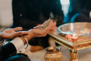 A hand adorned with henna holds dried herbs, a ritualistic offering beside a candle and metallic dish, symbolizing tradition and ceremony.