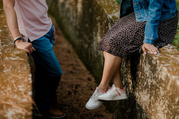 Two people are sitting on a stone bridge enjoying the outdoors in comfortable clothing, showcasing...