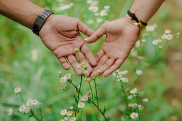Hands reaching over a field of wildflowers create a heart shape, showing a caring touch and...