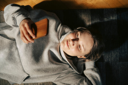 High angle view of young woman using smart phone while lying down with hand behind head