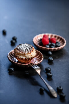 Dessert closeup &ndash; a cheesecake cupcake on a porcelain plate, accompanied by forest fruits on the table.