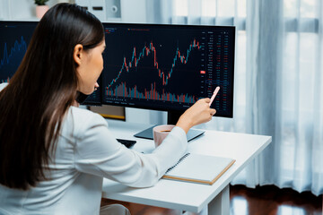 Young beautiful Asian businesswoman calling to broker, pointing with pen in increased exchange...