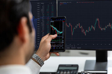 Trader businessman searching on smartphone, analyzing in dynamic stock exchange investment screen on pc with invest highest profitable financial technology market at modern home office. Surmise.