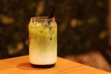 Matcha with strawberry puree, milk and ice. Refreshing sweet drink in a glass with a straw. Close-up of matcha. Drink on a table in a cafe or restaurant. Glass of strawberry green tea