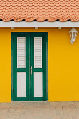 Bright yellow wall and contrasting green door with shutters create a striking entrance in a...
