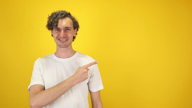 Smiling man pointing with index finger empty space, isolated on yellow studio background bold engaging visual ideal for advertising, personal branding, customer service, World Smile Day campaigns