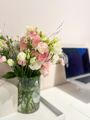 Fresh bouquet of pink and white flowers in a clear vase on a modern desk, with a laptop and minimalistic workspace in the background, enhancing the serene atmosphere