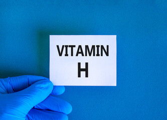 Vitamin H symbol. Concept words Vitamin H on beautiful white card. Doctor's hand in blue medical glove. Beautiful blue background. Medical healthy lifestyle Vitamin H concept.