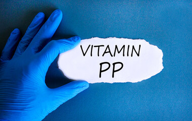 Vitamin PP symbol. Concept words Vitamin PP on beautiful white paper. Doctor's hand in blue medical glove. Beautiful blue background. Medical healthy lifestyle Vitamin PP concept.