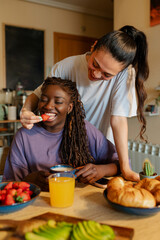 Two women are enjoying a healthy breakfast together at their kitchen table, sharing a moment of...