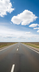 Fototapeta premium Empty asphalt road stretches into a vast, flat landscape under a vibrant blue sky dotted with fluffy clouds.