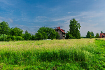 A scenic view of a rustic stone house with a red roof nestled among lush trees in a wide, grassy...