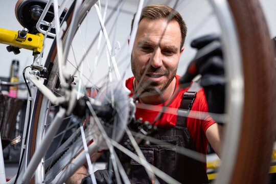 Experienced bicycle repairman adjusting gear shifter in modern bike workshop. - Powered by Adobe