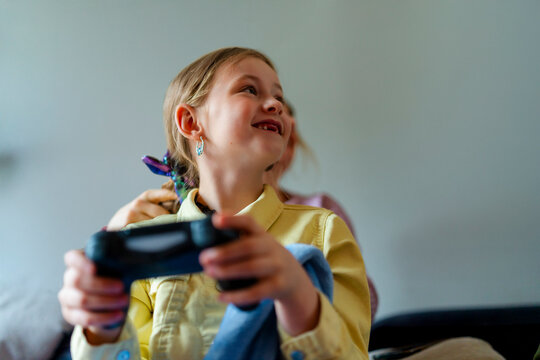 Low angle view of smiling girl looking away while holding game controller at home