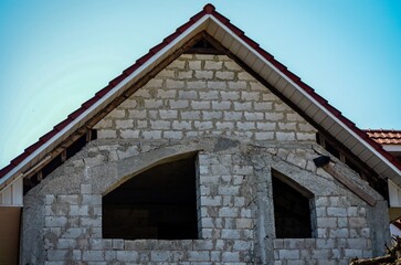 A house with a red roof and white bricks. The roof is slanted and the house is unfinished