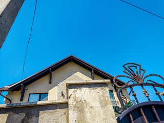 A house with a brown roof and a white wall. The roof is slanted and the house is surrounded by a fence