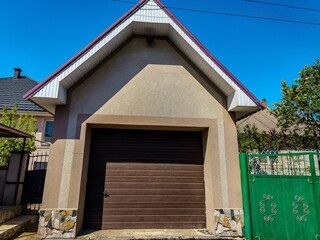 A brown garage door with a green gate in front of a house. The garage door is open and the gate is...