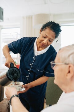 Mature female caregiver serving tea to elderly man in retirement home
