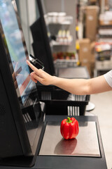 A woman buys bell peppers at a self-checkout. 